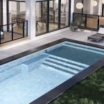 Piscine creusée en fibre de verre Mova, modèle 12x25 - Avec terrasse, finition Diamant couleur Mova, ambiance soirée éclairée